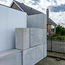 Gestapelde betonblokken vormen afscheiding naast gebouw en terrein met hekwerk